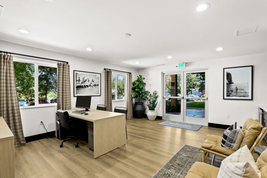 Interior entryway with double glass doors, potted plants, desk with computer, and a reception desk with computer.