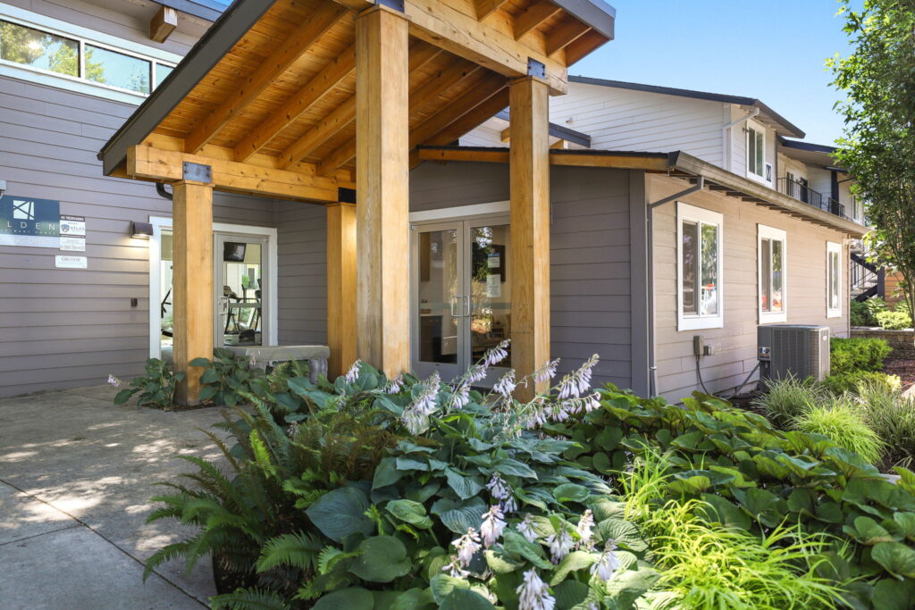 exterior view of leasing office with angled wooden gazebo over entrance and lush leaf vegetation