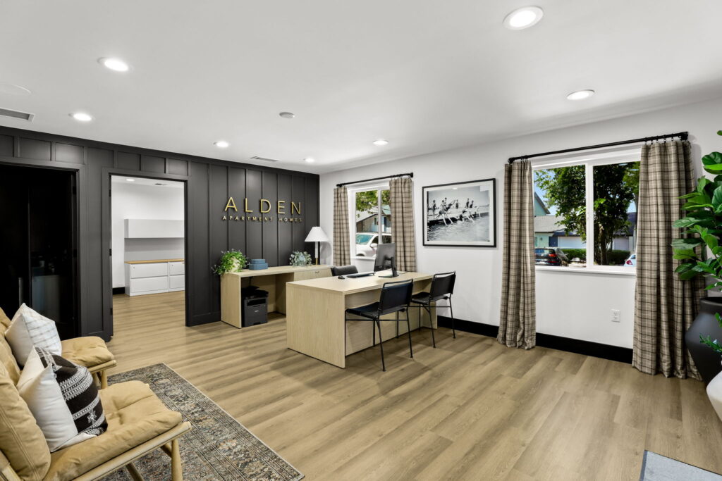 Leasing office interior with a desk and chairs, wood flooring, wall art, and a sign reading “Alden Apartment Homes.”
