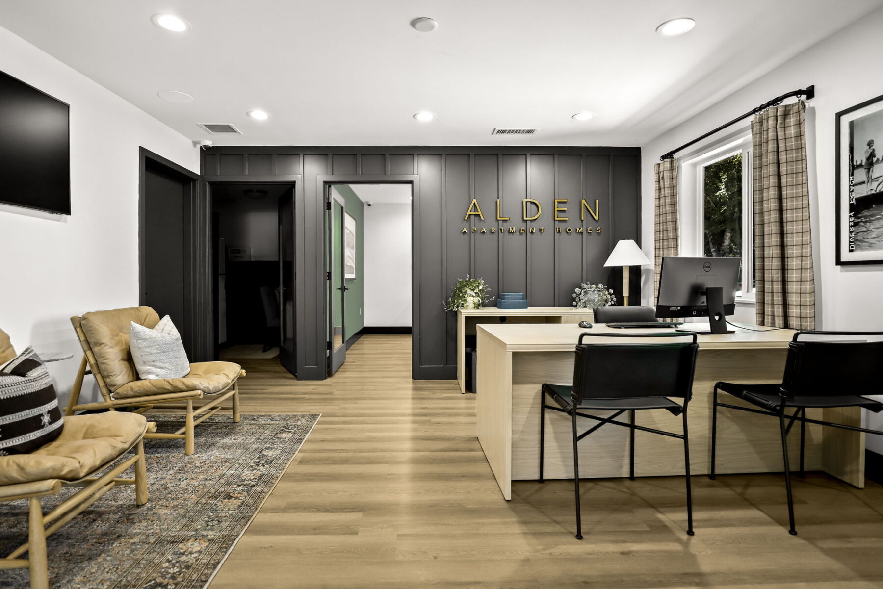 Leasing office interior with a desk and chairs, wood flooring, wall art, and a sign reading “Alden Apartment Homes.”